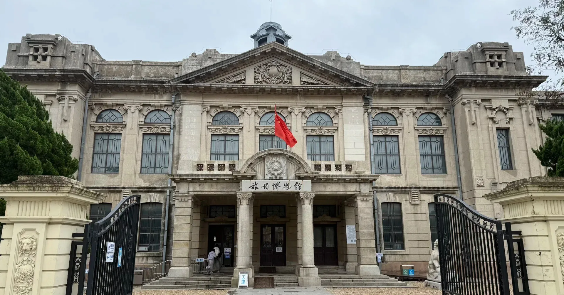Lushun (Port Arthur) Historic District,Dalian,Liaoning,Chinatravel Front view of a grand historic building with ornate stonework, large arched windows, and a Chinese flag at the entrance.
