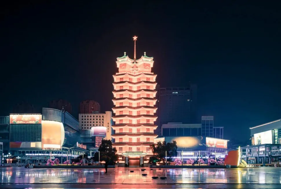 Erqi Memorial Tower,Zhengzhou,Henan,Chinaexplorertour Night view of a lit multi‑tiered pagoda tower in a city square, its warm glow reflected on the wet pavement.