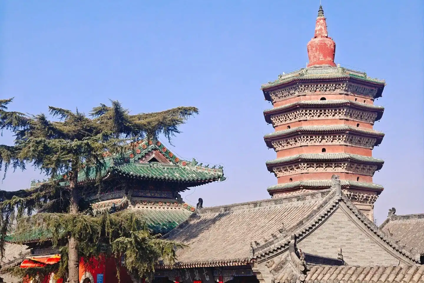 Wenfeng Pagoda,Anyang,Henan,Chinaexplorertour Seven-story red brick pagoda with green-tiled eaves stands beside traditional Chinese temple roofs under a clear blue sky.