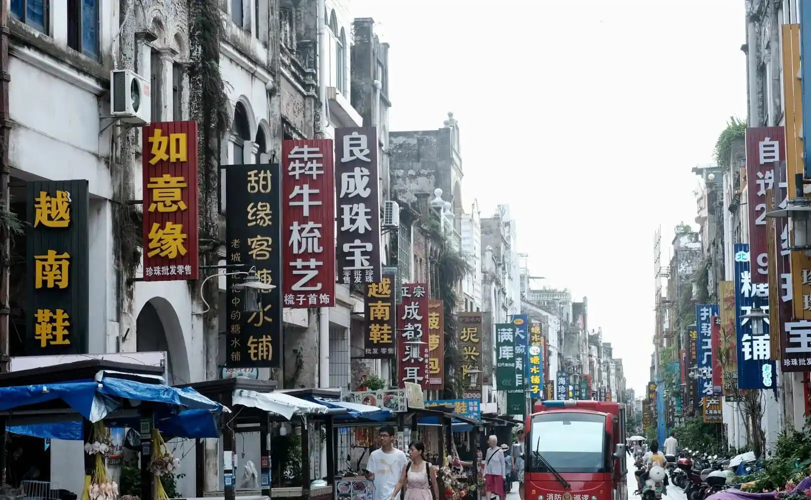 Beihai Old Street,Beiahi,Guangxi,Chinaexplorertour Busy street in China lined with tall vertical signs in Chinese characters and market stalls on both sides, with pedestrians and a red bus in the distance.
