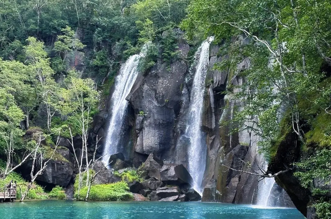 Baishan North Slope Scenic Area,Baishan,Jilin,Chinatravel Waterfall cascade over rocky cliff into a turquoise lake surrounded by green trees.