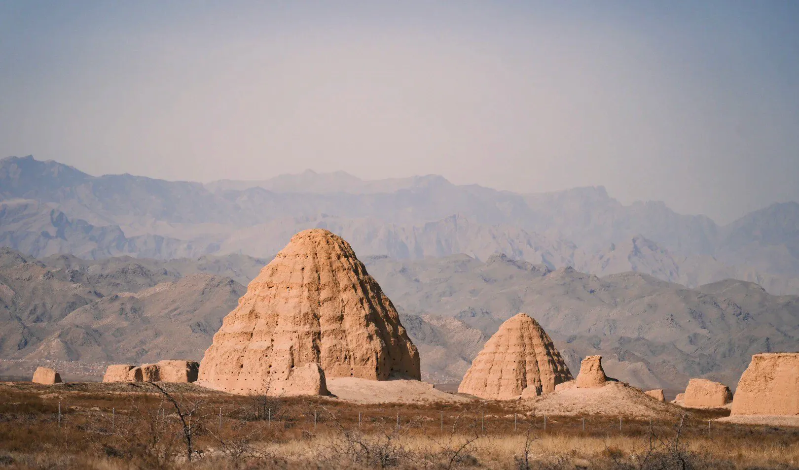 Western Xia Imperial Tombs,Yinchuan,Ningxia,Chinatravel Desert landscape with large earthen pyramidal structures in the foreground and distant mountains on the horizon.