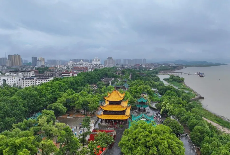 Yueyang Tower,Yueyang,Hunan,Chinaexplorertour Aerial view of a city with a bright yellow multi-tiered pagoda in a green park beside a wide river.
