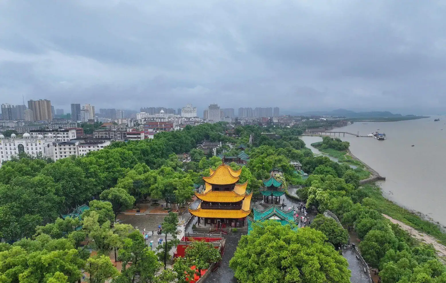 Yueyang Tower,Yueyang,Hunan,Chinaexplorertour Aerial view of a city with a bright yellow multi-tiered pagoda in a green park beside a wide river.