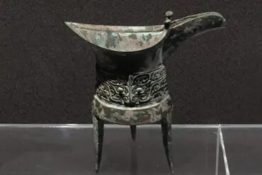 Zhengzhou Museum,Zhengzhou,Henan,Chinaexplorertour Ancient bronze ritual vessel with a long curved spout, standing on three legs, featuring ornate scrolling decorations around the middle.