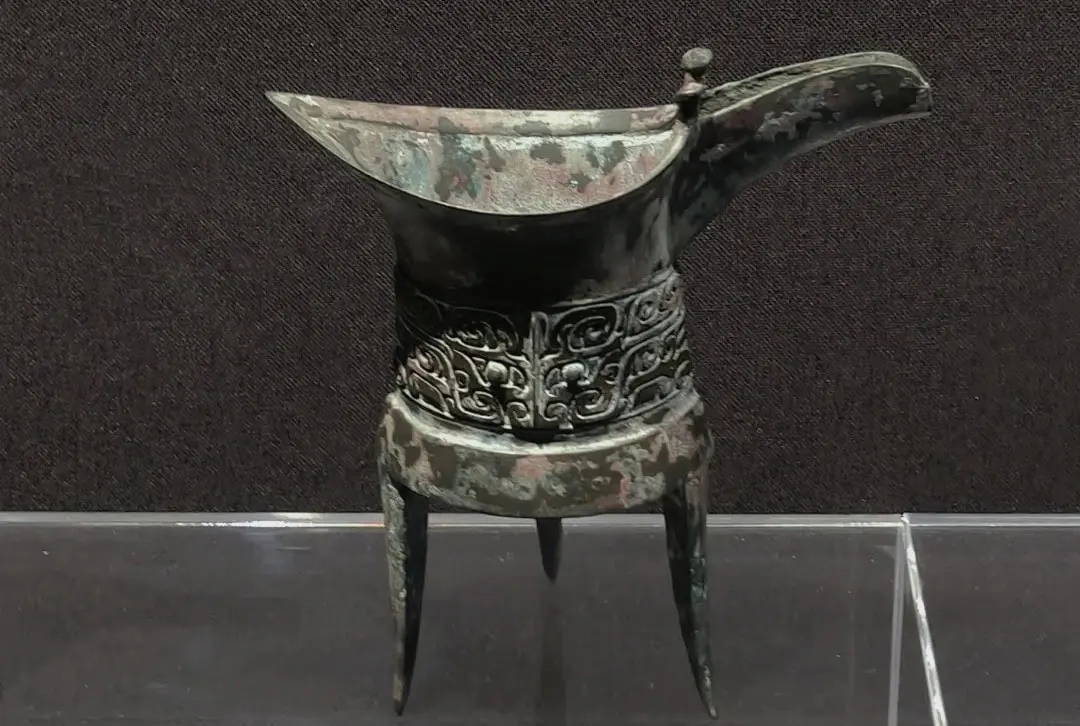 Zhengzhou Museum,Zhengzhou,Henan,Chinaexplorertour Ancient bronze ritual vessel with a long curved spout, standing on three legs, featuring ornate scrolling decorations around the middle.