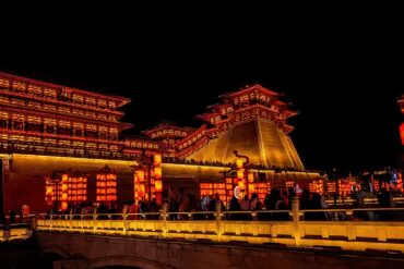 Yingtian Gate,Luoyang,Henan,Chinaexplorertour Night scene of a lit Chinese temple complex with red lanterns and a stone bridge, crowds along the railing.