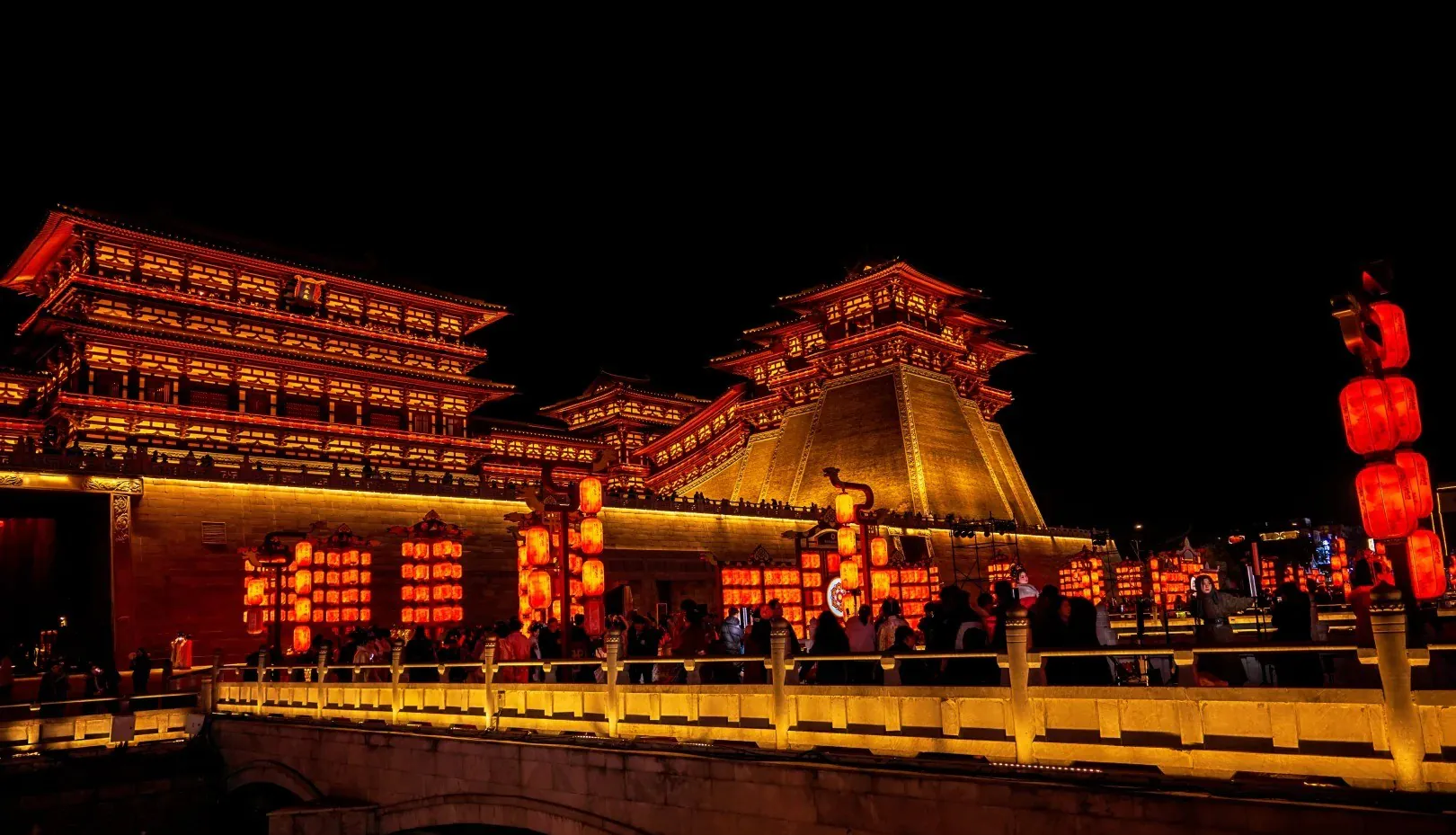 Yingtian Gate,Luoyang,Henan,Chinaexplorertour Night scene of a lit Chinese temple complex with red lanterns and a stone bridge, crowds along the railing.