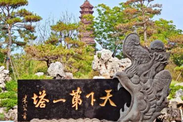 Kaifeng Iron Pagoda,Kaifeng,Henan,Chinatravel Dragon-carved stone sculpture holding a black plaque with golden Chinese characters; a pagoda and pine trees in a garden setting behind it.