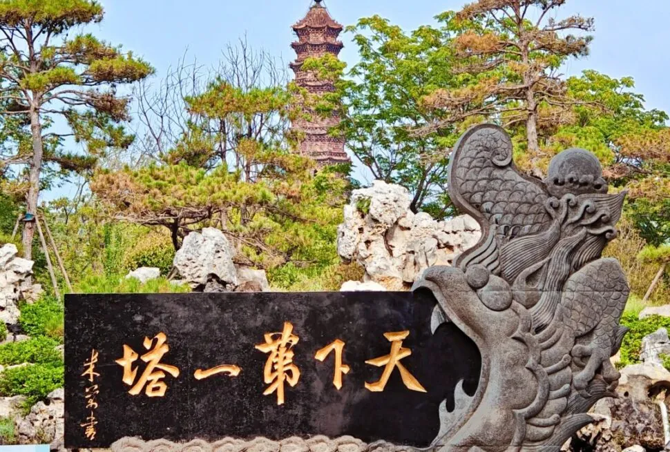 Kaifeng Iron Pagoda,Kaifeng,Henan,Chinatravel Dragon-carved stone sculpture holding a black plaque with golden Chinese characters; a pagoda and pine trees in a garden setting behind it.