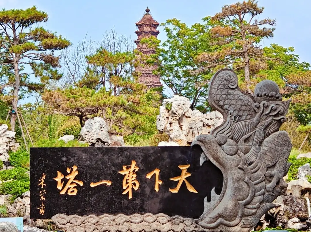 Kaifeng Iron Pagoda,Kaifeng,Henan,Chinatravel Dragon-carved stone sculpture holding a black plaque with golden Chinese characters; a pagoda and pine trees in a garden setting behind it.