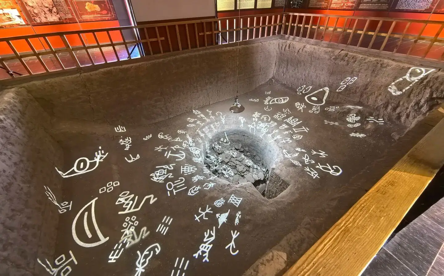 Yin Ruins (Yinxu, UNESCO),Anyang,Chinaexplorertour Indoor museum exhibit: a sunken rectangular pit with a central rock-filled hole, surrounded by white glyphs on the floor and a railing along the edge.