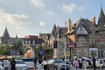 Russian Street (Zhongshan Square),Dalian,Liaoning,Chinatravel Busy urban street lined with ornate brick buildings with steep roofs; pedestrians cross near a traffic light against a blue sky.