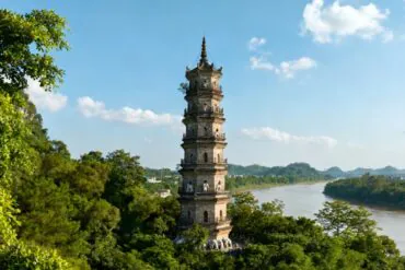 Qingxiu Mountain Ancient Pagoda,Nanning,Guangxi,Chinaexplorertour Tall multi-story pagoda rising through green trees beside a winding river on a clear day, blue sky above.