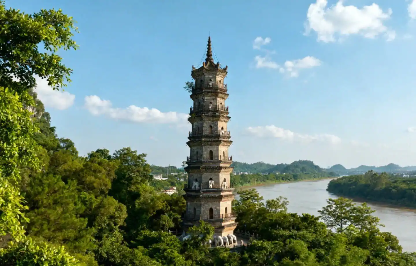 Qingxiu Mountain Ancient Pagoda,Nanning,Guangxi,Chinaexplorertour Tall multi-story pagoda rising through green trees beside a winding river on a clear day, blue sky above.