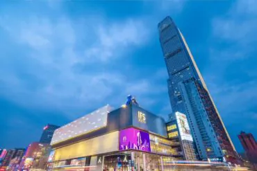 IFS International Finance Center Building,Changsha,Hunan,Chinaexplorertour Evening cityscape of a modern mall with bright signage and a tall glass skyscraper against a blue dusk sky.
