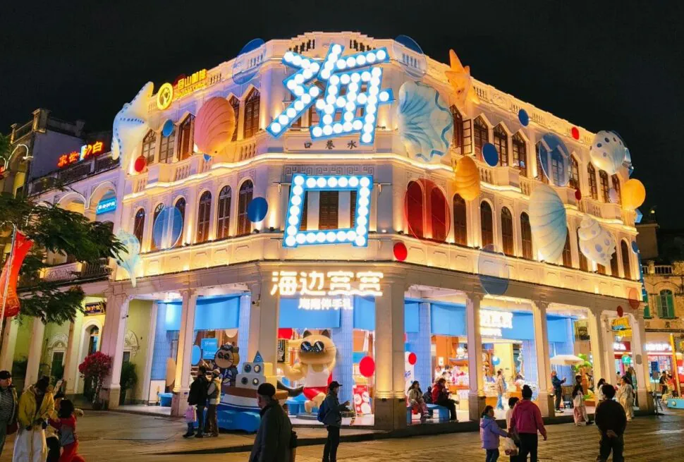 Qilou Old Street,Haikou,Hainan,Chinaexplorertour Bright, neon-lit seaside-themed storefront at night with large blue sign and balloons, people walking outside.