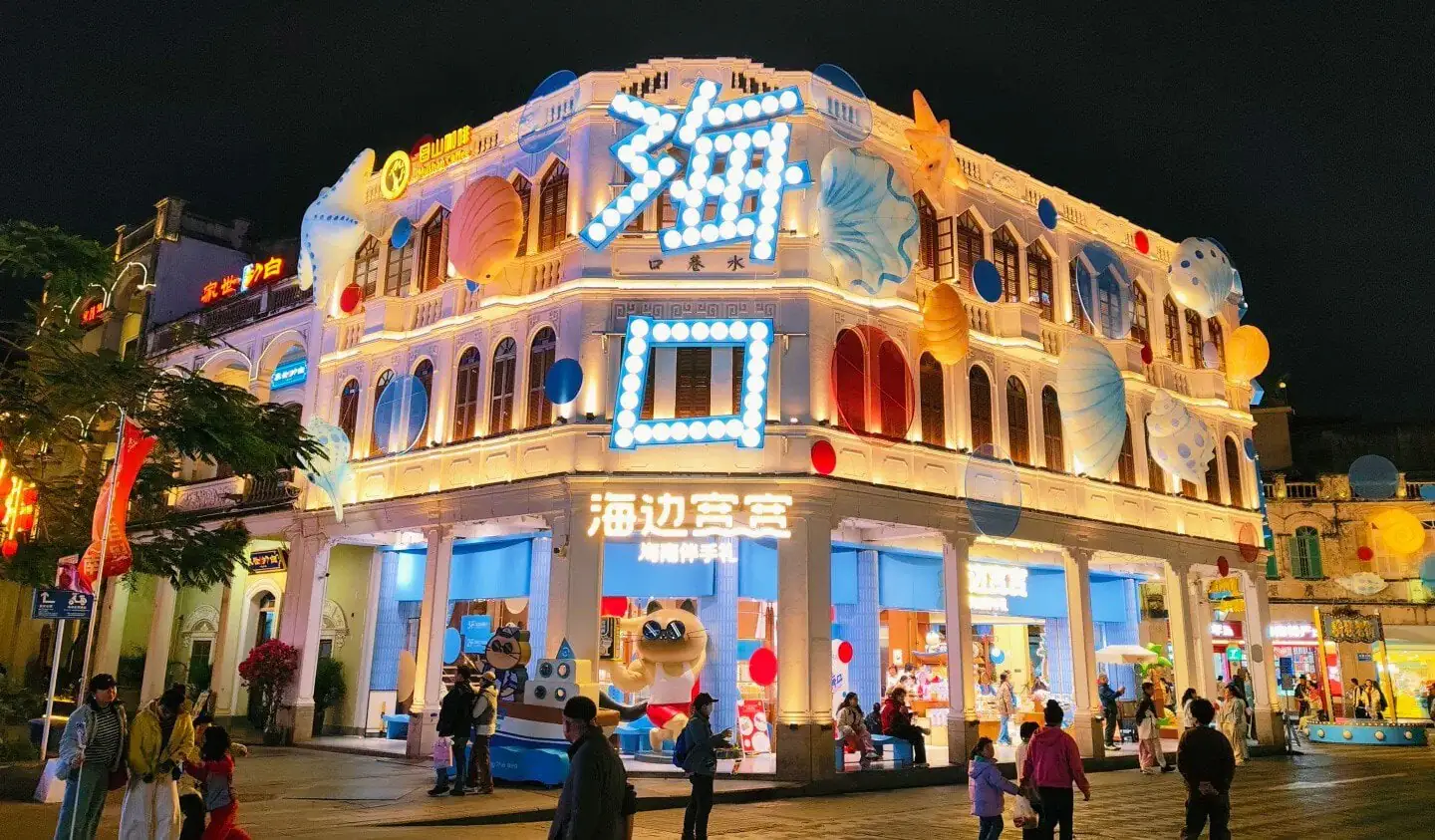 Qilou Old Street,Haikou,Hainan,Chinaexplorertour Bright, neon-lit seaside-themed storefront at night with large blue sign and balloons, people walking outside.