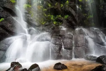 Wangtian'e Scenic Area,Baishan,Jilin,Chinatravel Waterfall cascading over dark basalt rocks with green moss, mist rising around a shallow pool at the base.