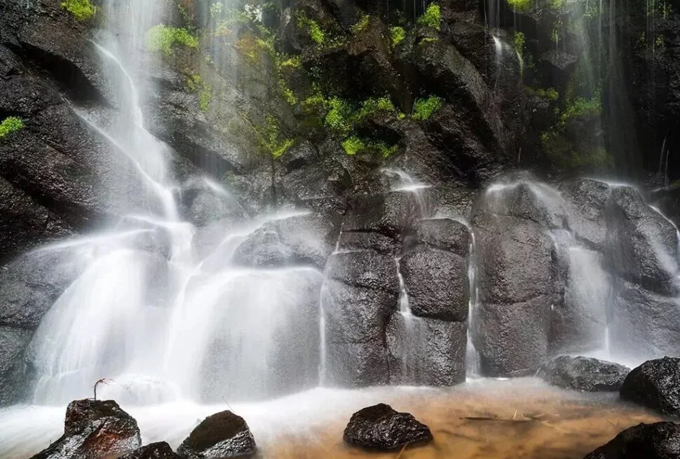 Wangtian'e Scenic Area,Baishan,Jilin,Chinatravel Waterfall cascading over dark basalt rocks with green moss, mist rising around a shallow pool at the base.