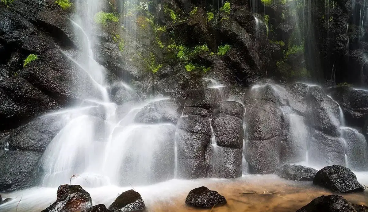 Wangtian'e Scenic Area,Baishan,Jilin,Chinatravel Waterfall cascading over dark basalt rocks with green moss, mist rising around a shallow pool at the base.