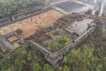 Southern Great Wall Ruins,Fenghuang,Hunan,Chinaexplorertour Aerial view of an old stone fortress with walls, stairways, and a central courtyard amid surrounding trees and hills.
