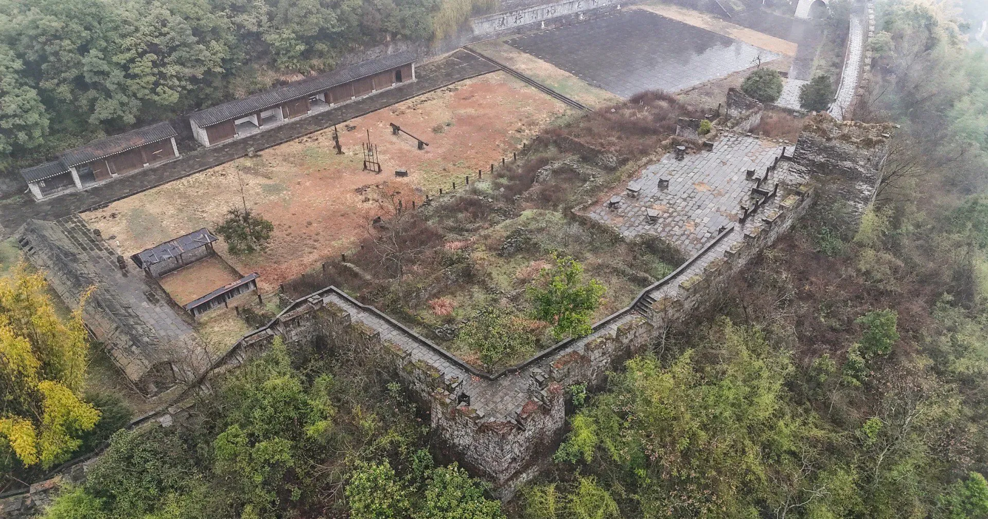 Southern Great Wall Ruins,Fenghuang,Hunan,Chinaexplorertour Aerial view of an old stone fortress with walls, stairways, and a central courtyard amid surrounding trees and hills.