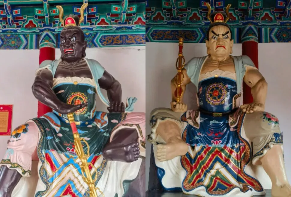 Daxiangguo Temple,Kaifeng,Henan,Chinatravel Two enormous guardian warrior statues in ornate robes and headdresses, seated indoors with a decorative ceiling above.