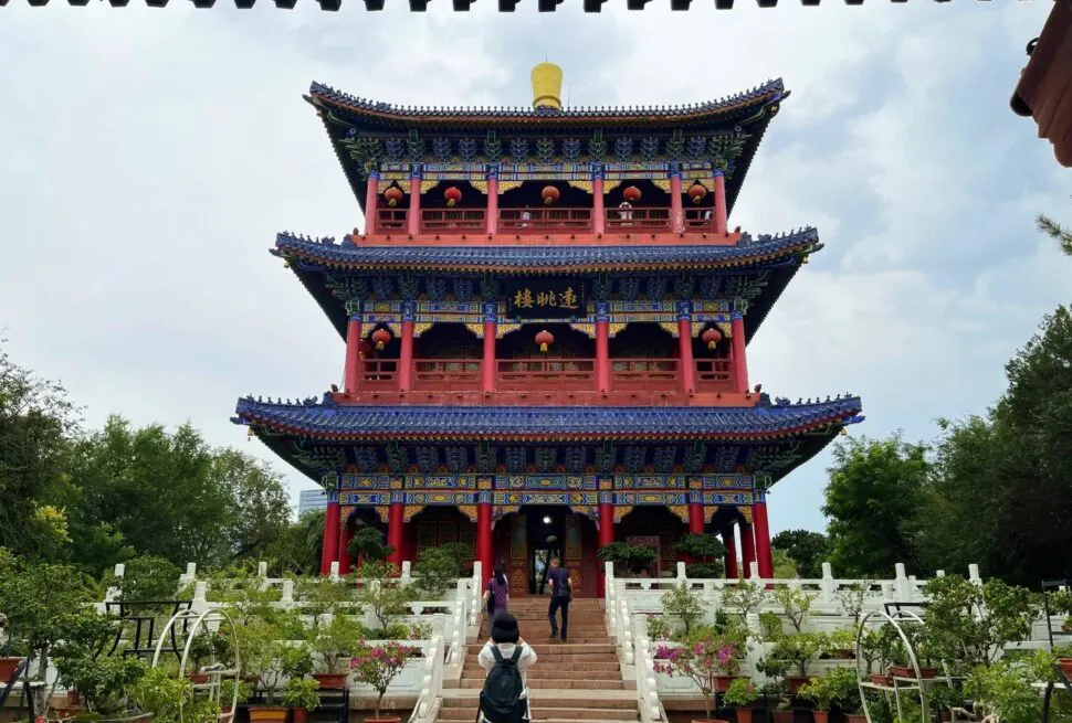 Red Hill Park,Urumqi,Xinjiang,Chinaexplorertour Three-story Chinese temple pavilion with blue roofs, red columns, and red lanterns in a garden front view.