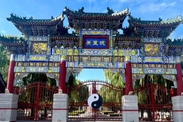 Youli Castle & Scenic Area,Anyang,Henan,Chinaexplorertour Ornate Chinese archway with blue plaque reading '美里城', intricate gold carvings, red pillars, and a yin-yang symbol hanging in front of a gated courtyard.