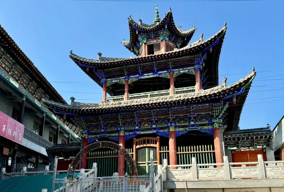 Shaanxi Mosque,Urumqi,Xinjiang,Chinaexplorertour Colorful, multi-tiered Asian temple with ornate blue-painted eaves and red columns against a clear blue sky.