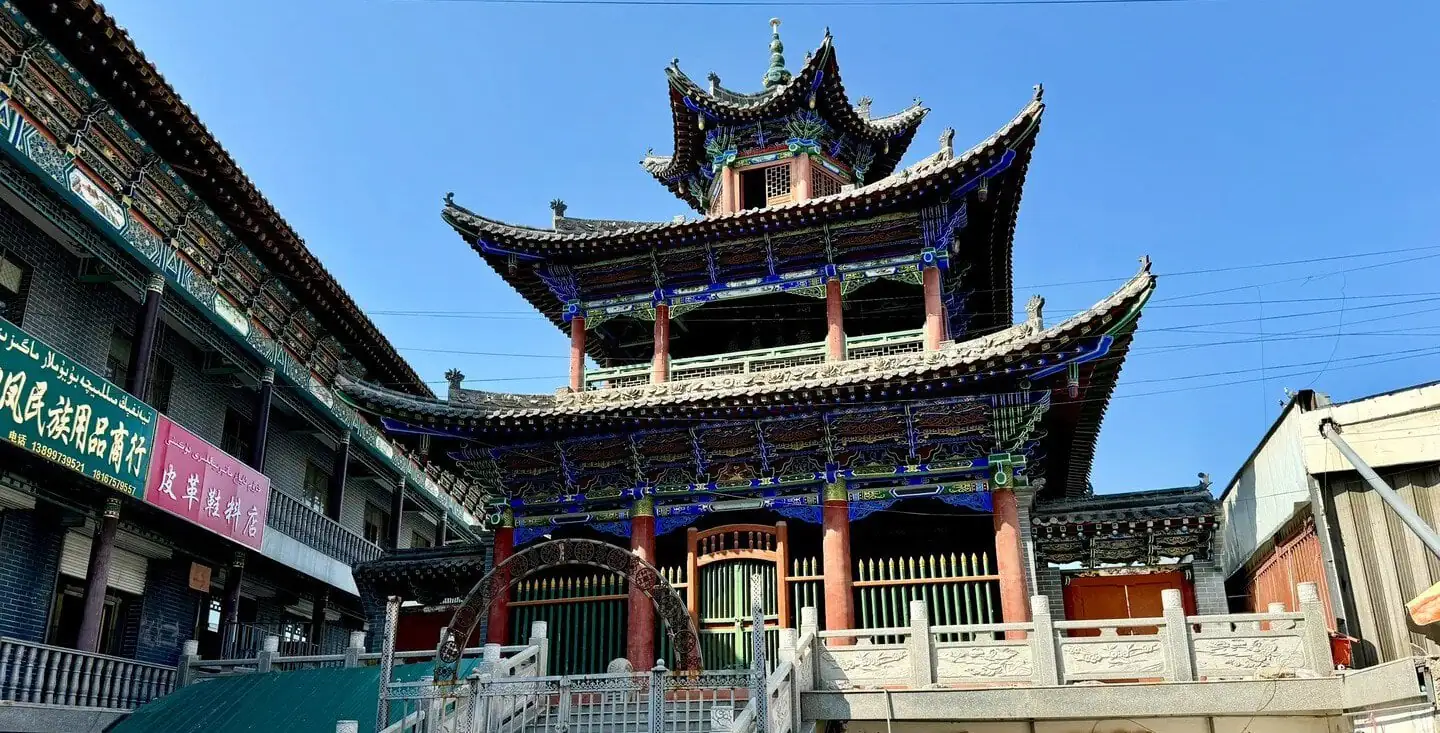 Shaanxi Mosque,Urumqi,Xinjiang,Chinaexplorertour Colorful, multi-tiered Asian temple with ornate blue-painted eaves and red columns against a clear blue sky.