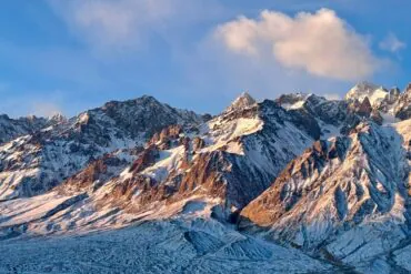 Pamir Plateau (Tashkurgan),Kashgat,China tour Snow-covered jagged mountain range under a blue sky with a few clouds.