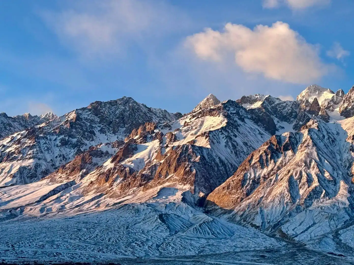 Pamir Plateau (Tashkurgan),Kashgat,China tour Snow-covered jagged mountain range under a blue sky with a few clouds.