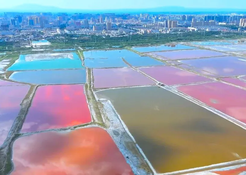 Aerial view of rainbow-colored salt evaporation ponds with a distant city skyline on the horizon.Salt Lake,Yuncheng, Shanxi