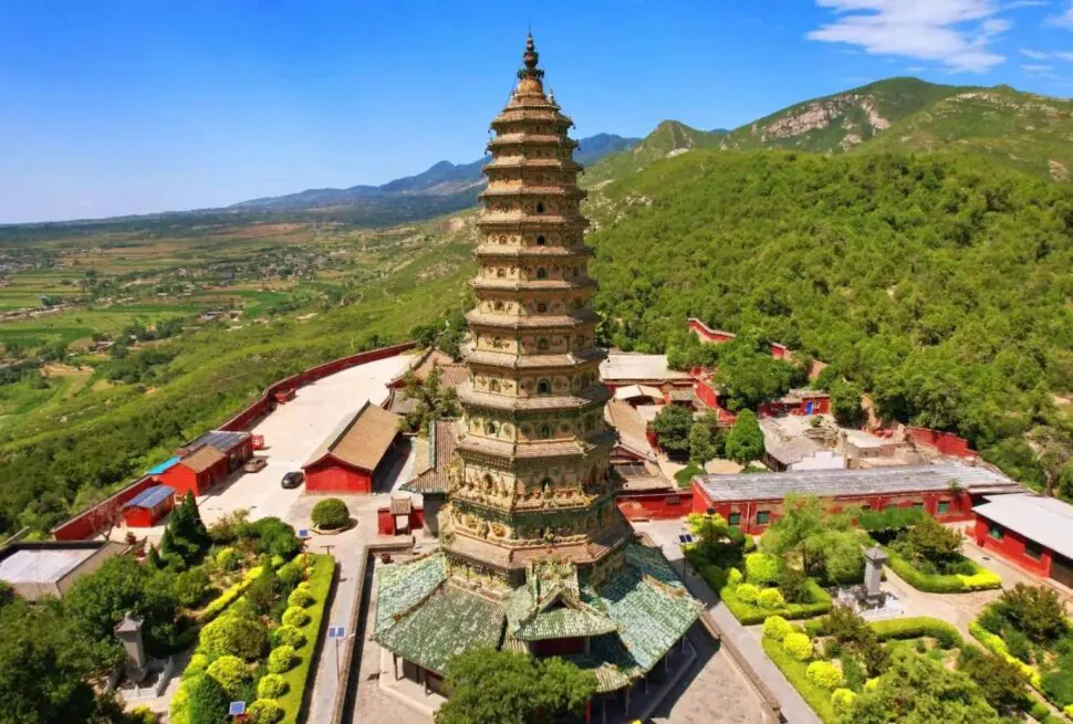 Tall multi-tiered pagoda surrounded by red temple buildings amid green hills and a valley under a blue sky,Guangsheng Temple,Linfen,Shanxi