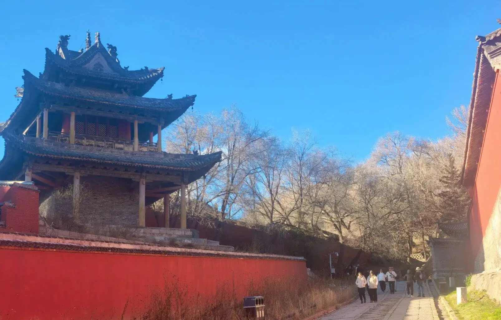 Traditional Chinese pavilion with curved roof in a park with trees and visitors.