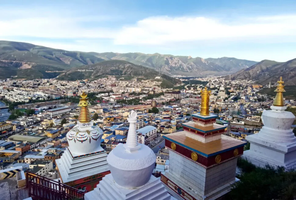view over a Tibetan town from a hillside with white stupas topped in gold, mountains in the distance under a blue sky,Jyeku Monastery,Yushu, Qinghai