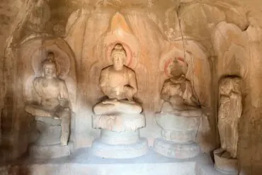 Stone cave shrine with a central seated Buddha flanked by two smaller statues, halos carved in the rock behind them for a devotional display.Tianlongshan Grottoes,Taiyuan, Shanxi