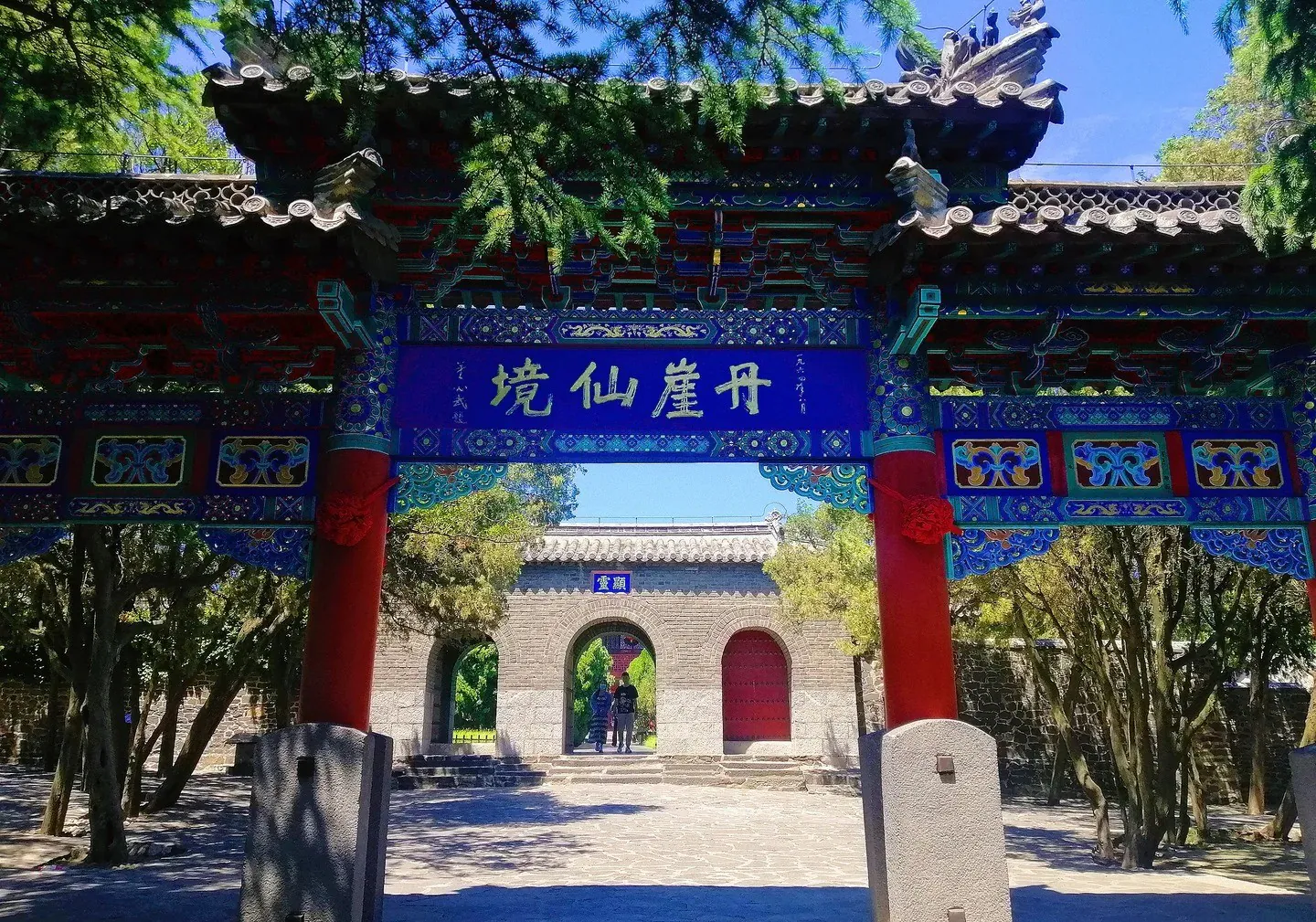 Ornate Chinese temple gate with red columns and blue decorative beams, leading to a brick archway and courtyard,Penglai Pavilion,Yantai,Shandong,Chinatravel