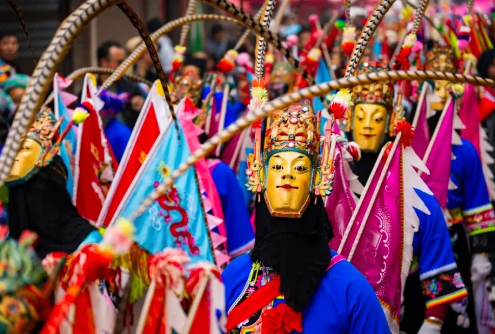 Masked performer in a bright blue outfit with a gold ornate mask leads a colorful festival parade.Anshun Tunpu Cultural Scenic Area ,Anshun,Guizhou