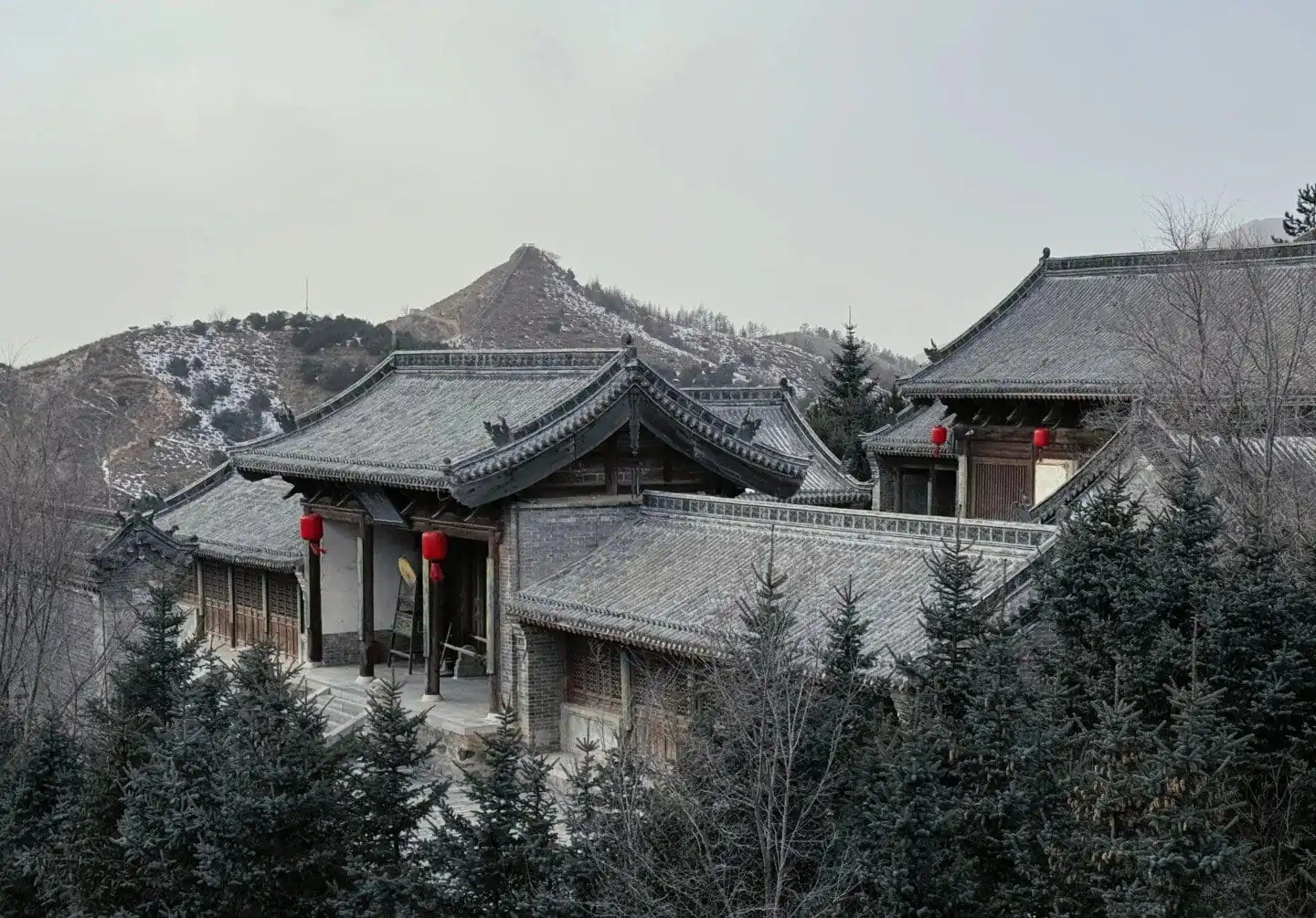 Ancient Chinese architecture with snow-covered roofs and surrounding trees.