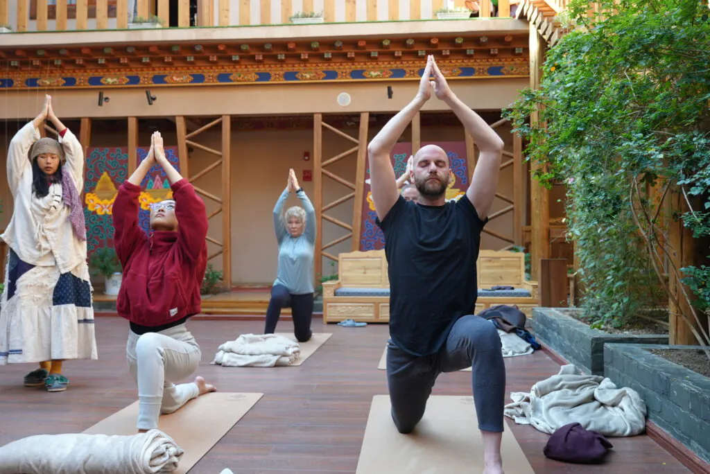 A group of people practicing yoga outdoors at a cultural site in China, with traditional wooden arch.