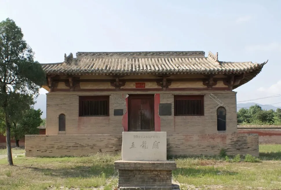 Traditional Chinese brick building with a tiled, curved roof and red central doorway, set in a grassy yard with a stone pedestal in front.Guangrenwang Temple,Yuncheng,Shanxi