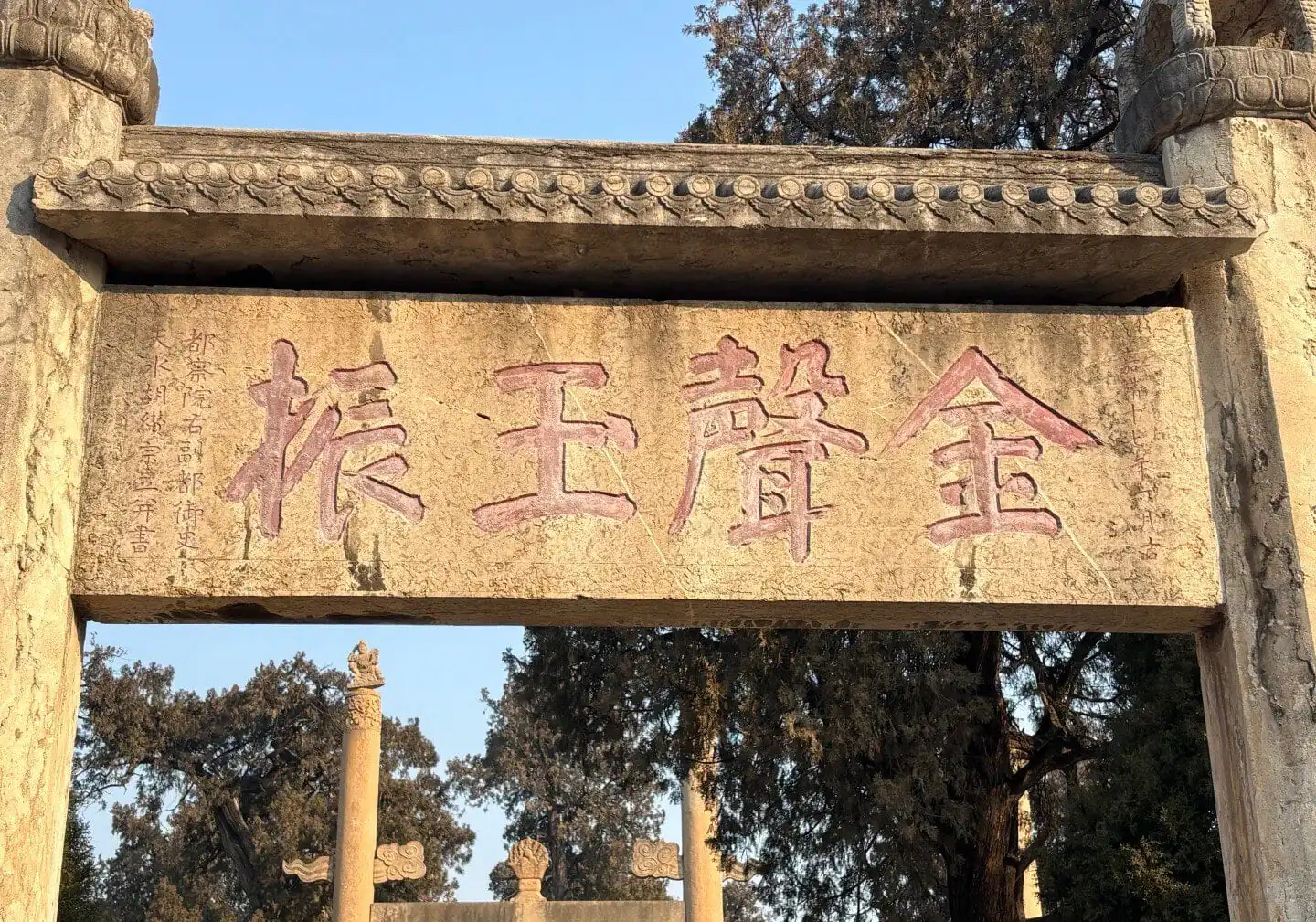 Ancient Chinese stone archway with engraved Chinese characters and trees in the background.