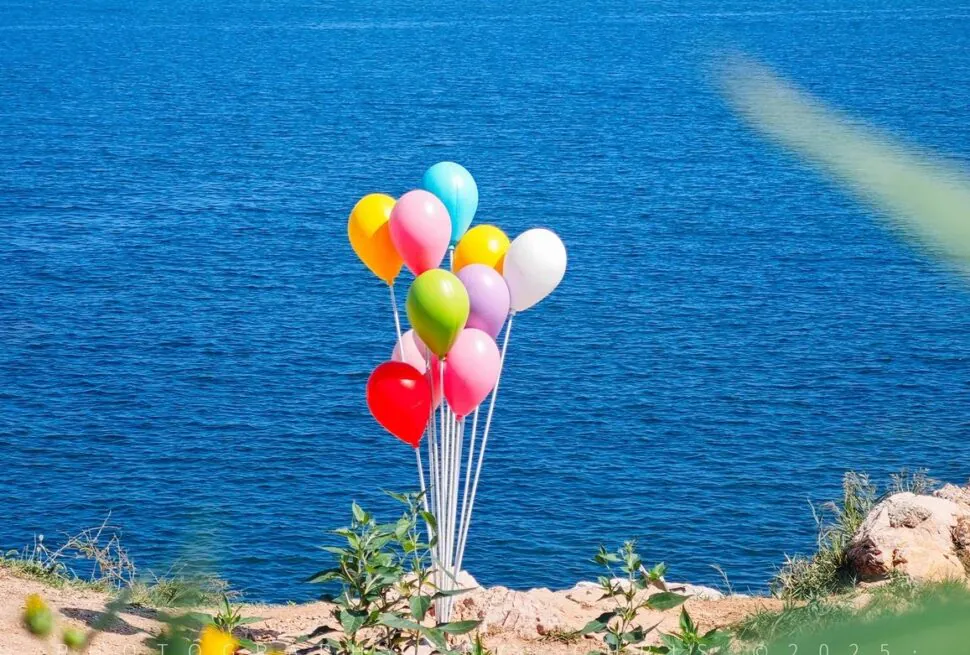 Cluster of colorful balloons tied to a weight on a rocky lakeshore with blue water in the background,Yangma Island,Yantai,Shandong,Chinatravel