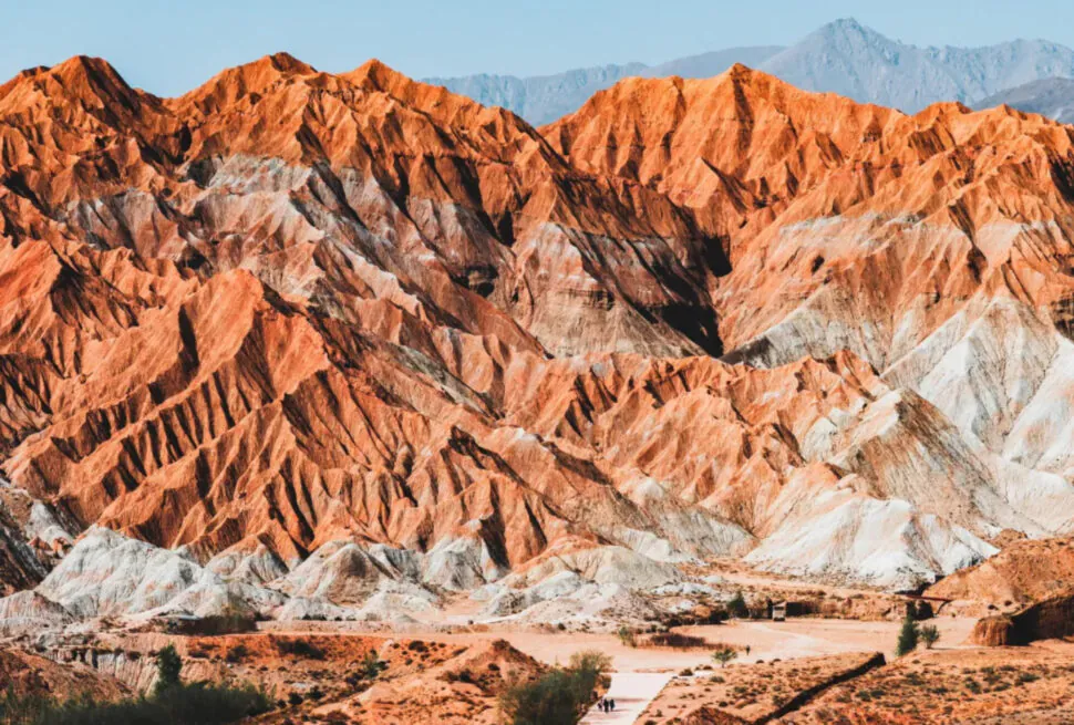 Ridge of orange-red striped mountains with a light path and hikers in the foreground under a blue sky,National Geopark,Hainan Prefecture,Qinghai ,Chinatravel