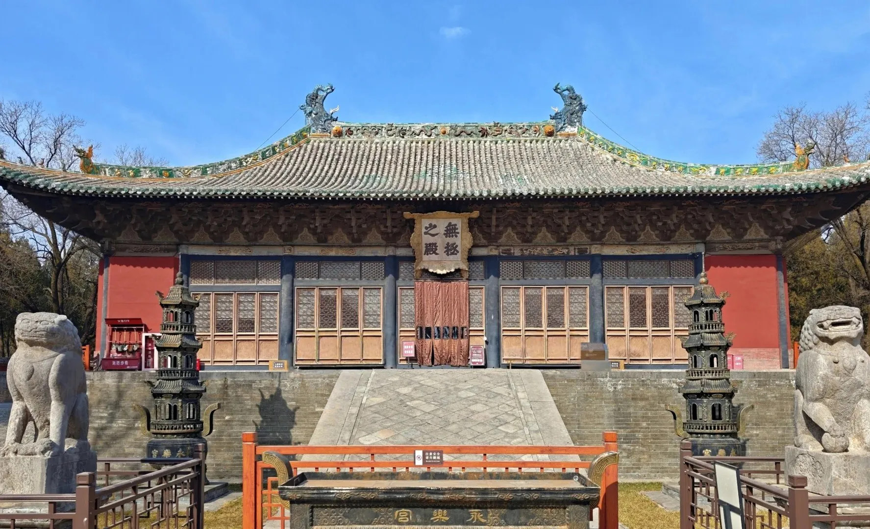 Traditional Chinese temple facade with ornate tiled roof, wooden doors, and stone guardian lions in front.Yongle Palace,Yuncheng,Shanxi