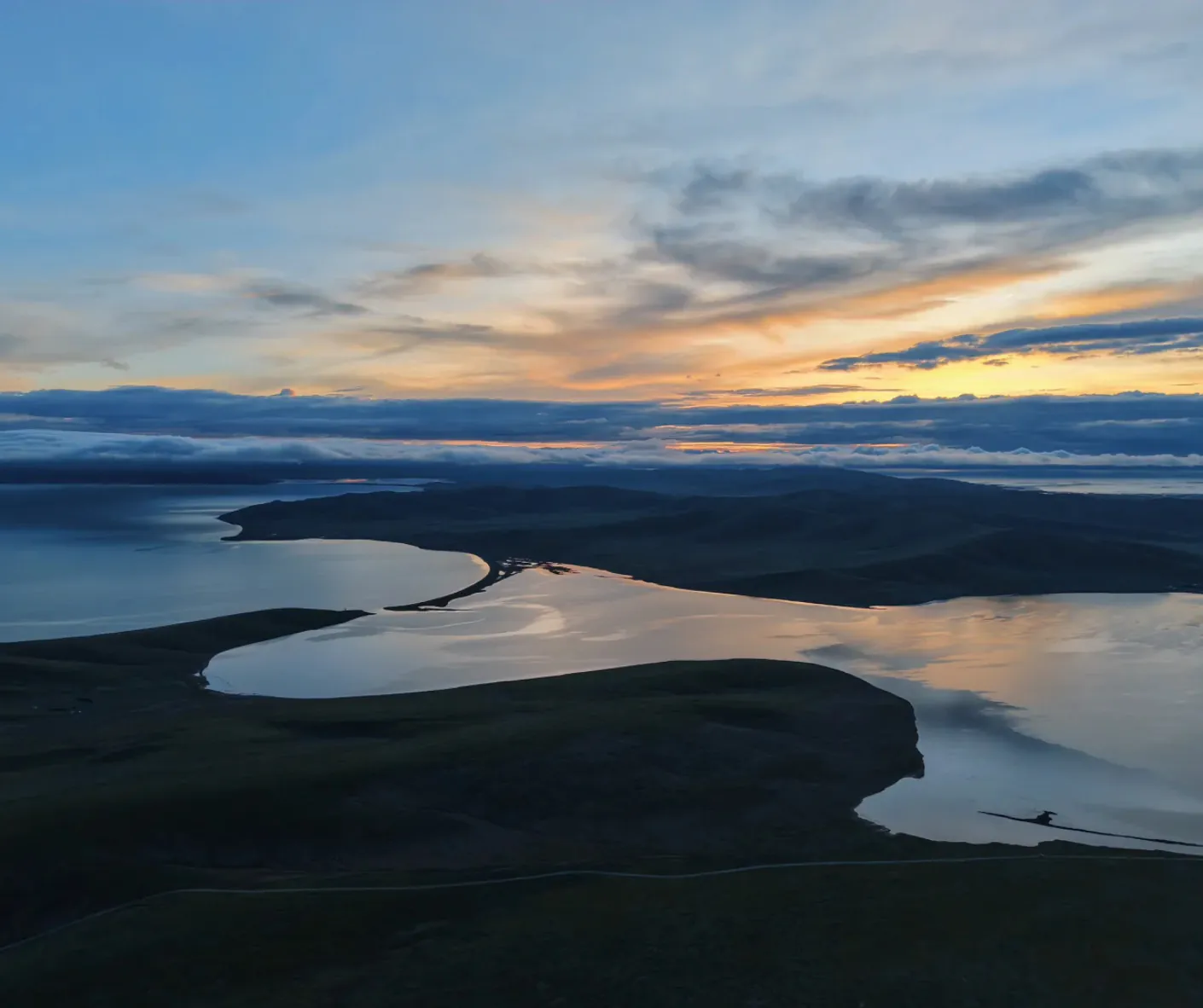 Aerial view of a winding river delta at sunset, reflecting orange and blue skies on calm water.Zaling Lake & Eling Lake,Yushu, Qinghai