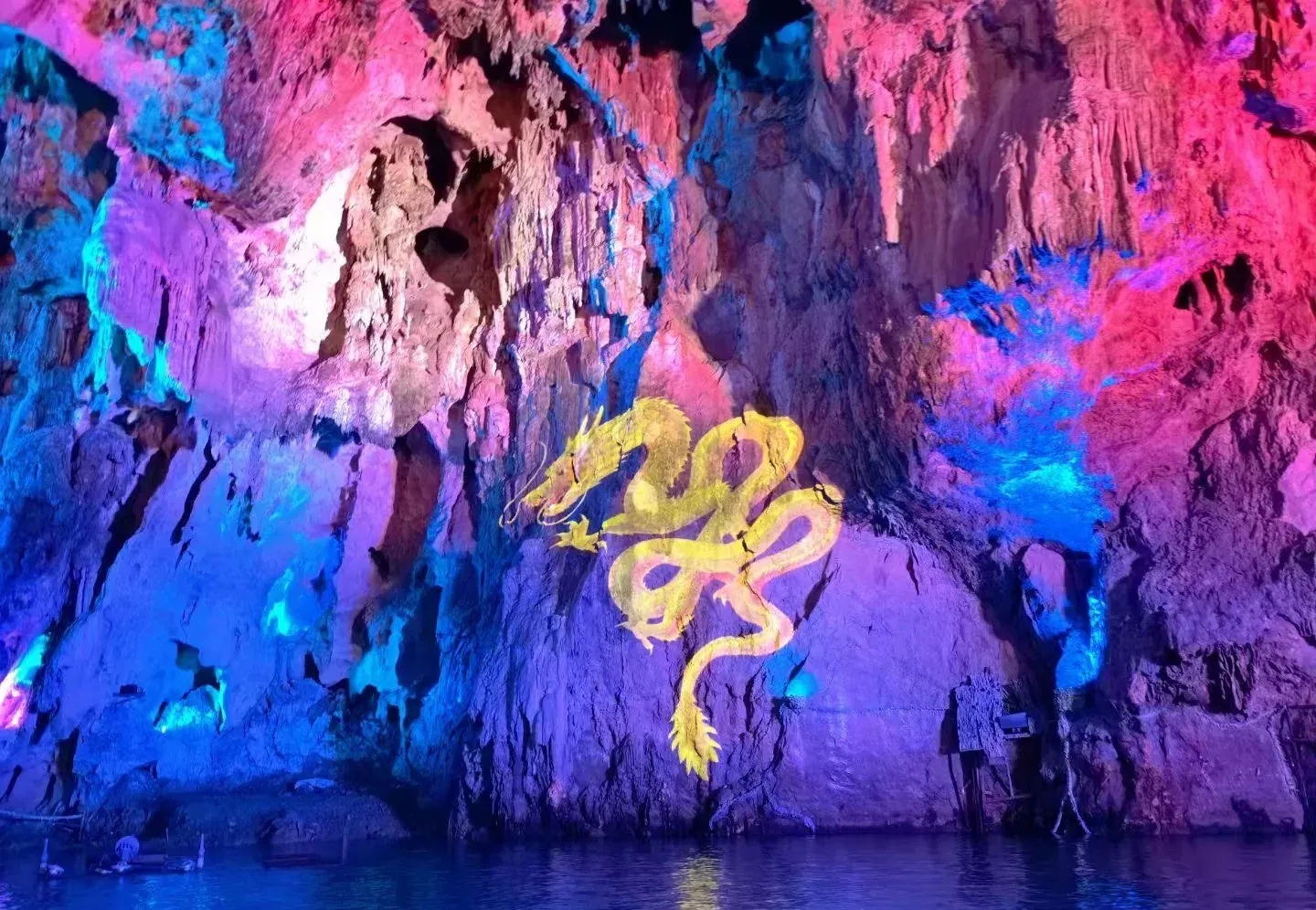 Cave wall illuminated in pink and blue with a yellow dragon mural painted on the rock, reflected in the water below.Dragon Palace Scenic Area ,Anshun,Guizhou